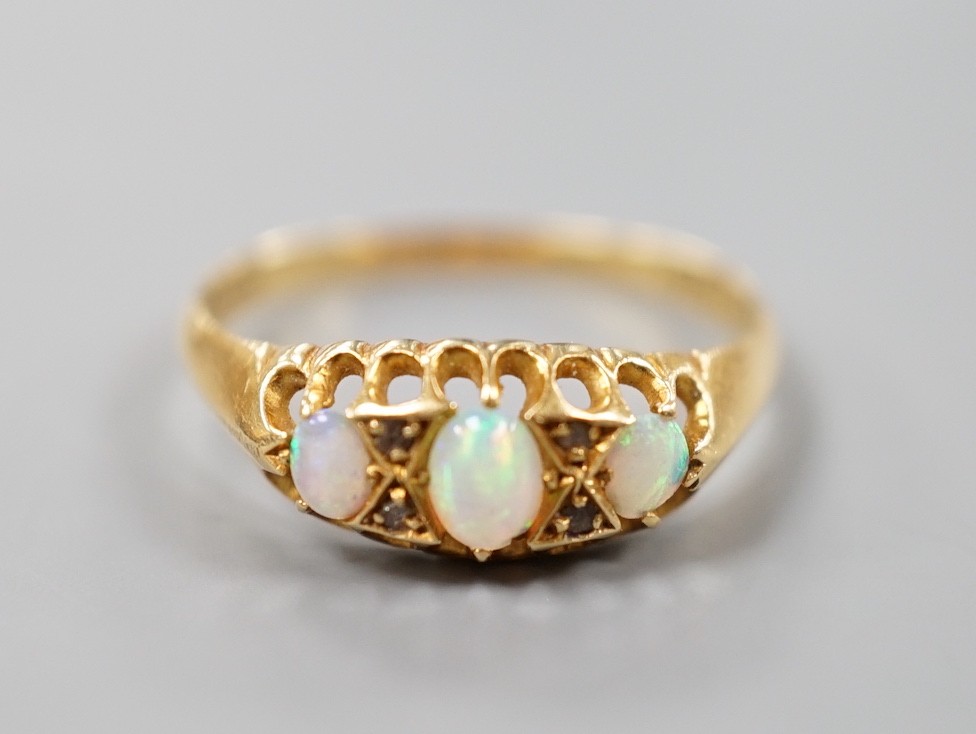 A George V 18ct gold and three stone white opal set half hoop ring, with diamond chip spacers, size O, gross weight 2.4 grams.